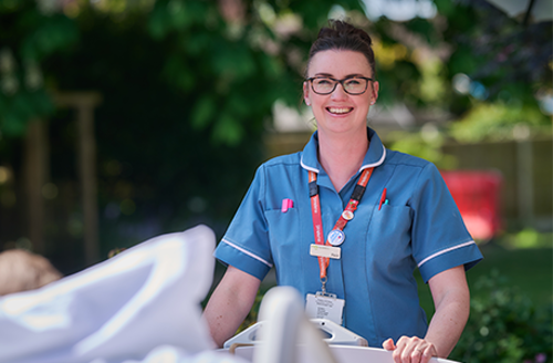 St Helena healthcare professional in a blue uniform standing beside a hospital bed in a garden setting.