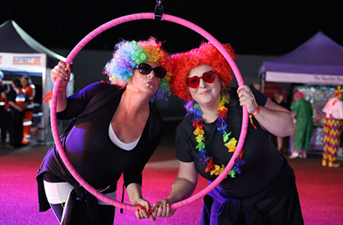 Two people wearing colourful wigs and sunglasses pose together inside a large pink hoop at St Helena Hospice's final Midnight Walk.
